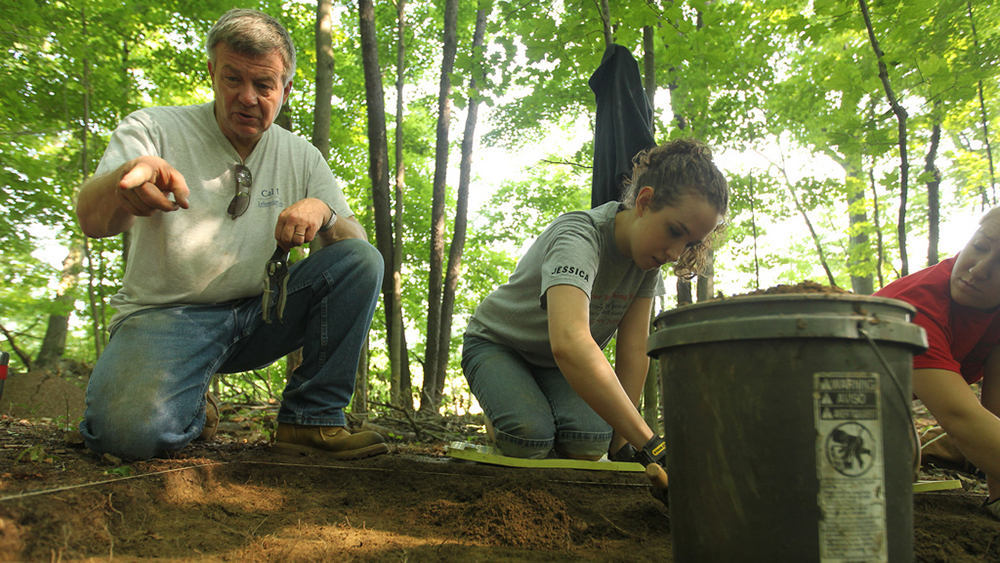 An archeaology professor instructs student in the field.