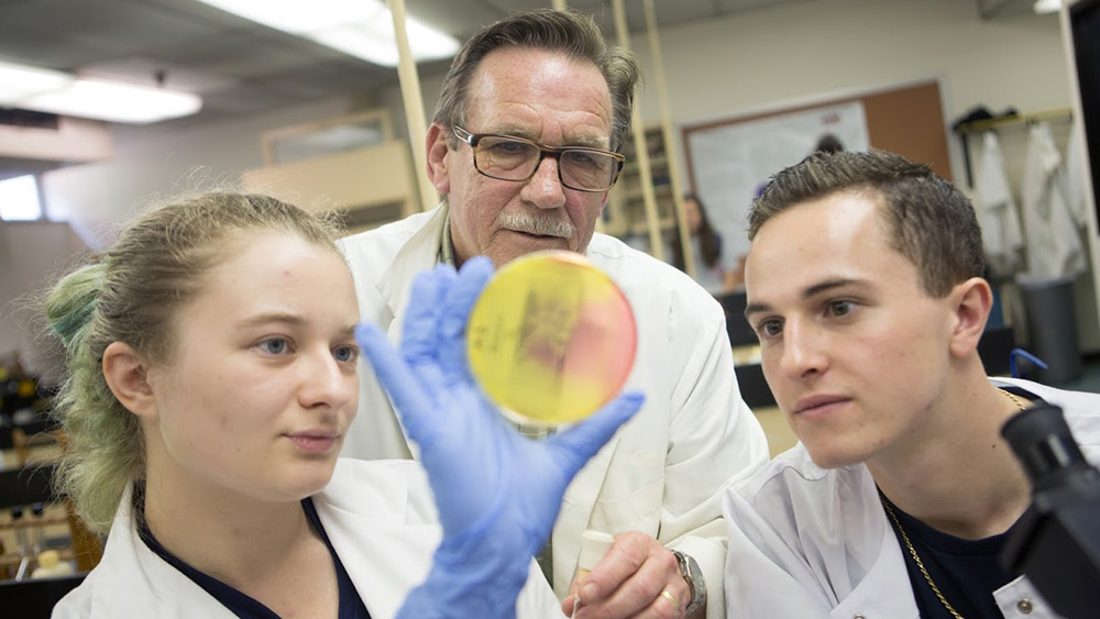Cal U students in a biology lab observe a specimen on a Petri dish.