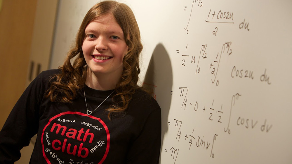 A student stands against a marker board with equations written on it.