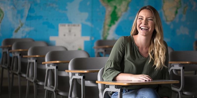 Cal U student laughs in classroom with world map.